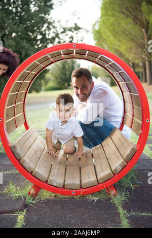 Father watching son playing in circular swing in park Stock Photo