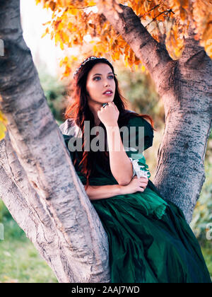 beautiful young woman in green vintage dress sitting in a tree Stock Photo