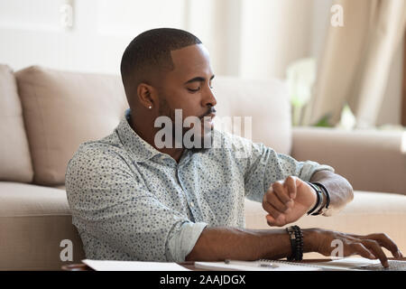 Worried african American male check time working on laptop Stock Photo
