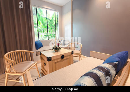 Phuket, Thailand - 7 November 2019 : Living zone in Craft resort & Villas room, have some furniture and flower vase on table with soft yellow light Stock Photo