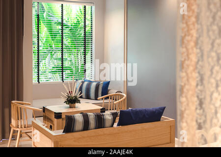 Phuket, Thailand - 7 November 2019 : Living zone in Craft resort & Villas room, have some furniture and flower vase on table with soft yellow light Stock Photo