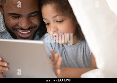 Loving biracial dad watch cartoons on tablet with daughter Stock Photo