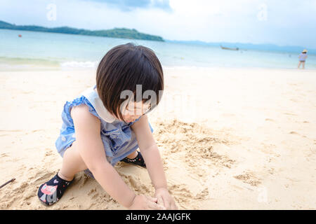 Phuket, Thailand - 12 June 2018: little girl playing sand making something on her mind near seaside
