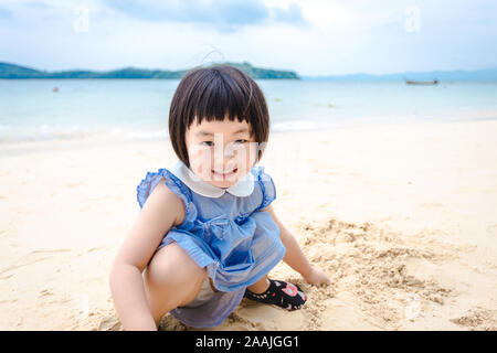 Phuket, Thailand - 12 June 2018: little girl playing sand with smile near seaside