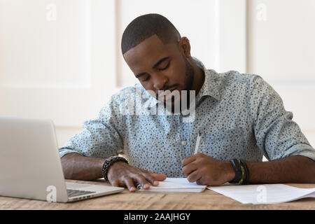 Focused african American male studying at laptop making notes Stock Photo