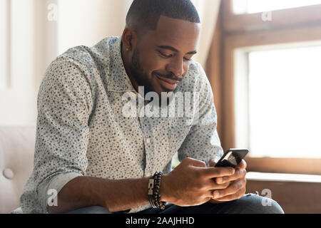 Smiling african American man feel happy texting on smartphone Stock Photo