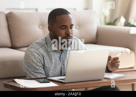 Focused biracial man studying at laptop making notes Stock Photo