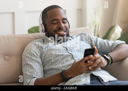 Happy biracial man listen to music resting on couch Stock Photo