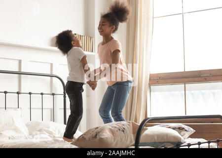 Mixed-race brother and sister holding hands jumping on bed Stock Photo