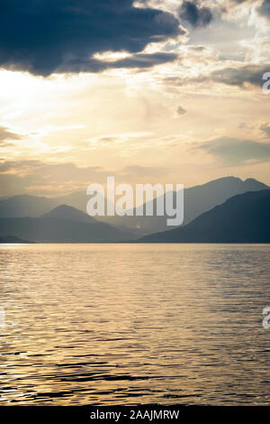 A sunset view of the Italian Alps over the calm waters of Lake Garda, Italy, at dusk. Stock Photo
