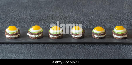 Canape with cream cheese, guacamole and fried quail eggs on the plate Stock Photo