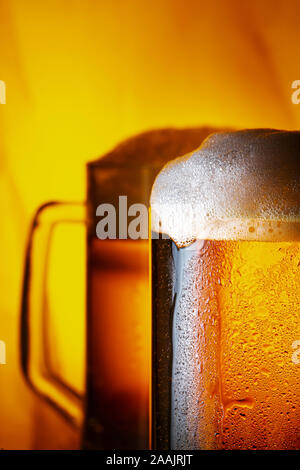 Two Light Beer Mugs with White Foam on Dark Wooden Table and Yellow Background Stock Photo