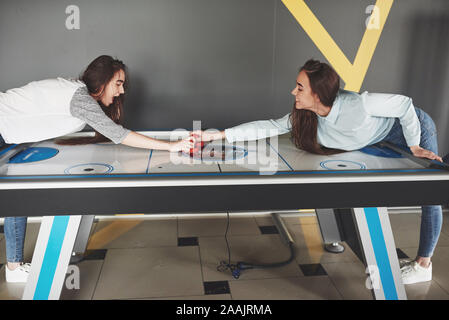Two beautiful twin girls play air hockey in the game roomand have fun Stock Photo