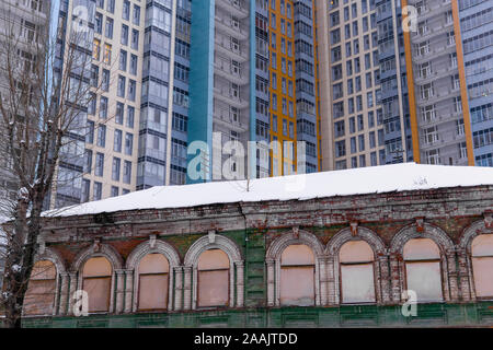 abandoned historic building with boarded up windows on the background of a modern apartment building Stock Photo
