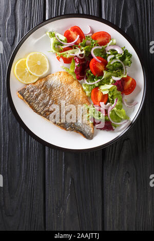 Fried gilt-head fish fillet with a side dish of vegetable salad close-up on a plate on the table. Vertical top view from above Stock Photo
