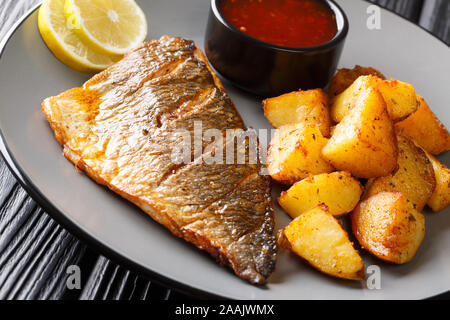 Fried gilt-head fish fillet with a side dish of potatoes and sauces close-up on a plate on the table. horizontal Stock Photo