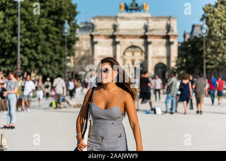 A beautiful female tourist in front of the Arc de Triomphe du Carrousel, situated at the entrance of Jardin de Tuileries, close to the beautiful build Stock Photo