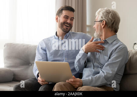Happy son and old father having fun, using laptop together Stock Photo