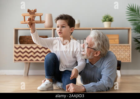 Happy grandfather and little grandson playing with wooden plane toy Stock Photo