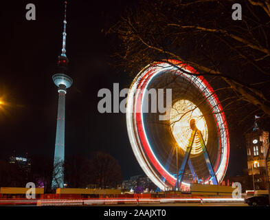 Berlin, Germany - December 12, 2018: Spinning illuminated Ferris Wheel at Christkindlmarkt (Christmas market) in Central Berlin. Fernsehturm Televisio Stock Photo