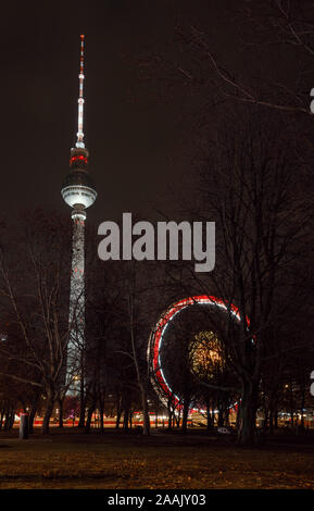 Berlin, Germany - December 12, 2018: Spinning illuminated Ferris Wheel and Fernsehturm Television Tower seen thru trees in Central Berlin Stock Photo