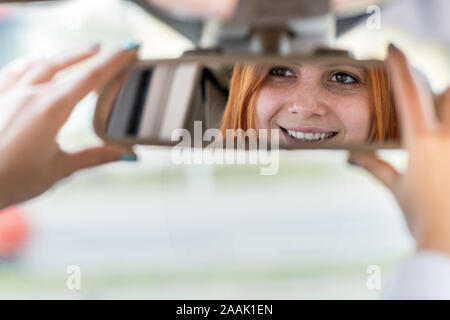 Young woman driver checking rear view mirror looking backwards while driving a car. Stock Photo