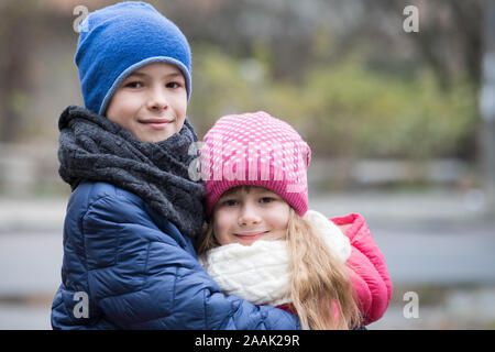 Two children boy and girl hugging each other outdoors wearing warm clothes in cold autumn or winter weather. Stock Photo