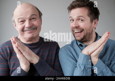 Tricky mature father and son smiling mysteriously, clasping hands, scheming something, keeping secret Stock Photo