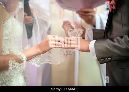 The bridal is wearing the wedding ring on her husband finger in church, meaning they are getting married as couple Stock Photo