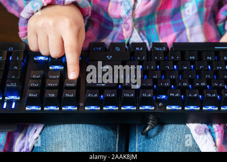 child holds a black keyboard on his lap and presses the delete key with his index finger Stock Photo