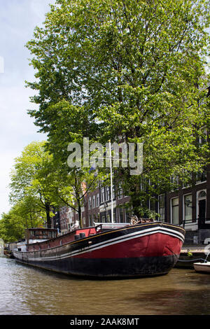 View of canal, boat house, trees and historical, traditional buildings showing Dutch architectural style in Amsterdam. It is a sunny summer day. Stock Photo