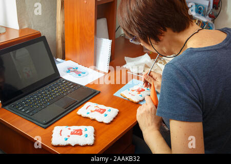 A young girl is engaged in decorating gingerbread cookies. Christmas and New Year gifts and the manufacture of gingerbread cookies for Christmas Stock Photo