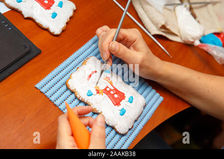 A young girl is engaged in decorating gingerbread cookies. Christmas and New Year gifts and the manufacture of gingerbread cookies for Christmas Stock Photo