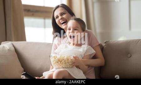 Smiling mom and little daughter watch movie eating popcorn Stock Photo