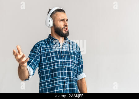 Freestyle. Guy wearing headphones in checkered shirt standing isolated on white listening music singing song joyful Stock Photo