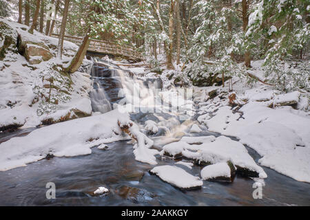 After the first snowfall of the season, water runs under a footbridge and falls over the canadian shield rocks of Potts Falls in Muskoka. Stock Photo