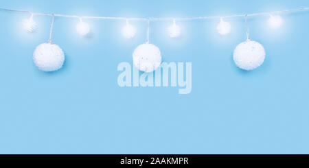 Christmas ornaments on cyan blue background. Festive decorations, white sparkling baubles and glowing lights garland. Traditional winter holiday celeb Stock Photo