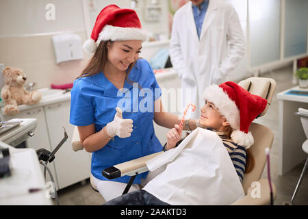 Dentist woman in Santa hat examining tooth young patient in ambulant. Stock Photo