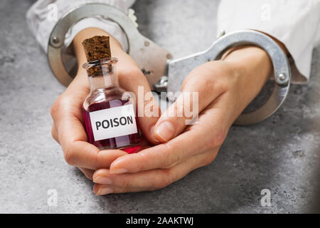 The detention of an employee of a chemical laboratory for the illegal production of toxic substances. Handcuffed hands with a bottle of poison Stock Photo