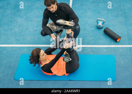 Fit young woman doing stretching exercises after training with personal fitness trainer. Stock Photo