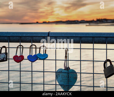 Love locks attached to a railing with a sunset in the distance. Concept of sun setting on a relationship, falling out of love and breaking up. Stock Photo
