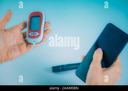 Woman measuring blood glucose levels, using smart phone to follow results. Stock Photo