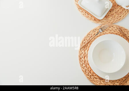 White ceramic tableware, fibre braided round placemat and cutlery set on white background. Scandinavian style. Stock Photo