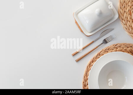 White ceramic tableware, fibre braided round placemat and cutlery set on white background. Scandinavian style. Stock Photo