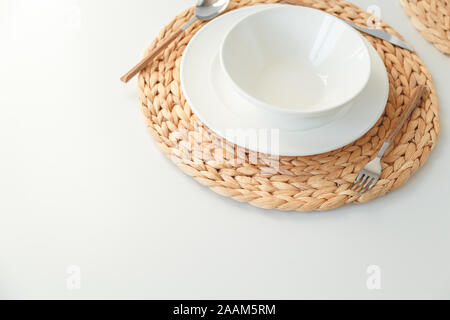 White ceramic tableware, fibre braided round placemat and cutlery set on white background. Scandinavian style. Stock Photo
