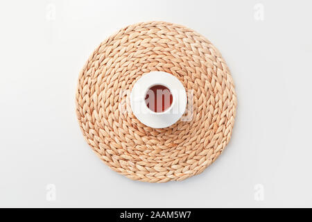 Cup of tea on round braided fibre placemat isolated on white, top view. Stock Photo