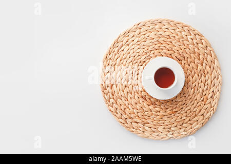 Cup of tea on round braided fibre placemat isolated on white, top view. Stock Photo