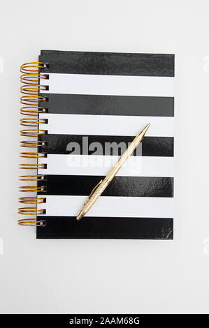 Diary striped black and white book with gold ring binders and a shiny gold pen writing instrument isolated on a light background.  Great for business Stock Photo