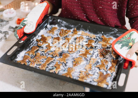 Closeup of woman holding baking tray full of tasty Christmas gingerbread cookies Stock Photo