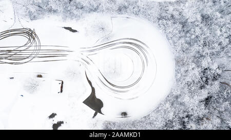 A drone / aerial view of a road covered with snow and ice. Lines have carved out by the cars driving through. Stock Photo